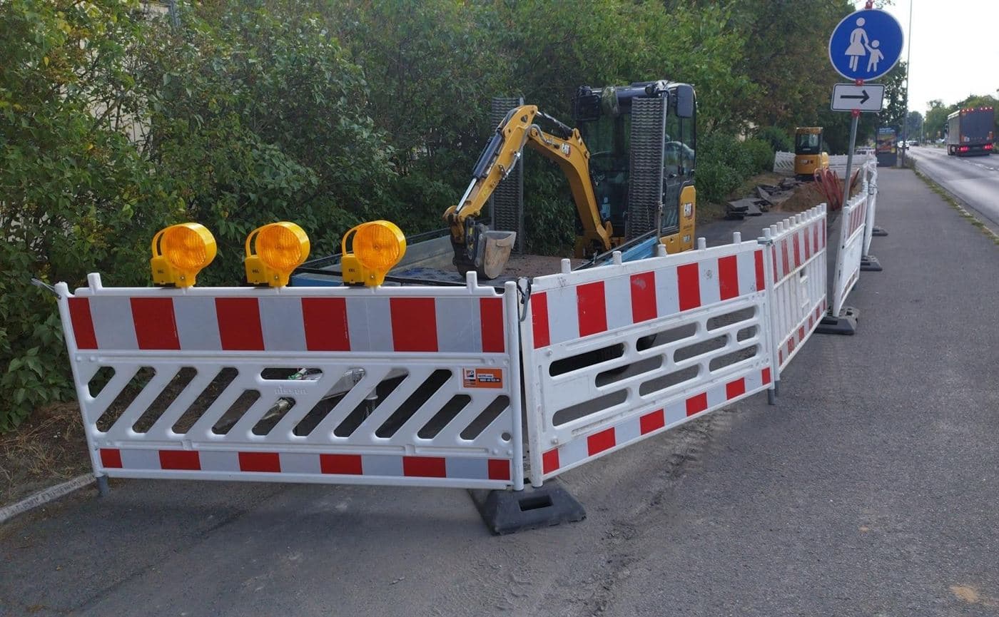 Abgesperrter Arbeitsbereich mit Minibagger und Warnleuchten neben einem Gehweg an der Kötzschenbroder Straße in Dresden